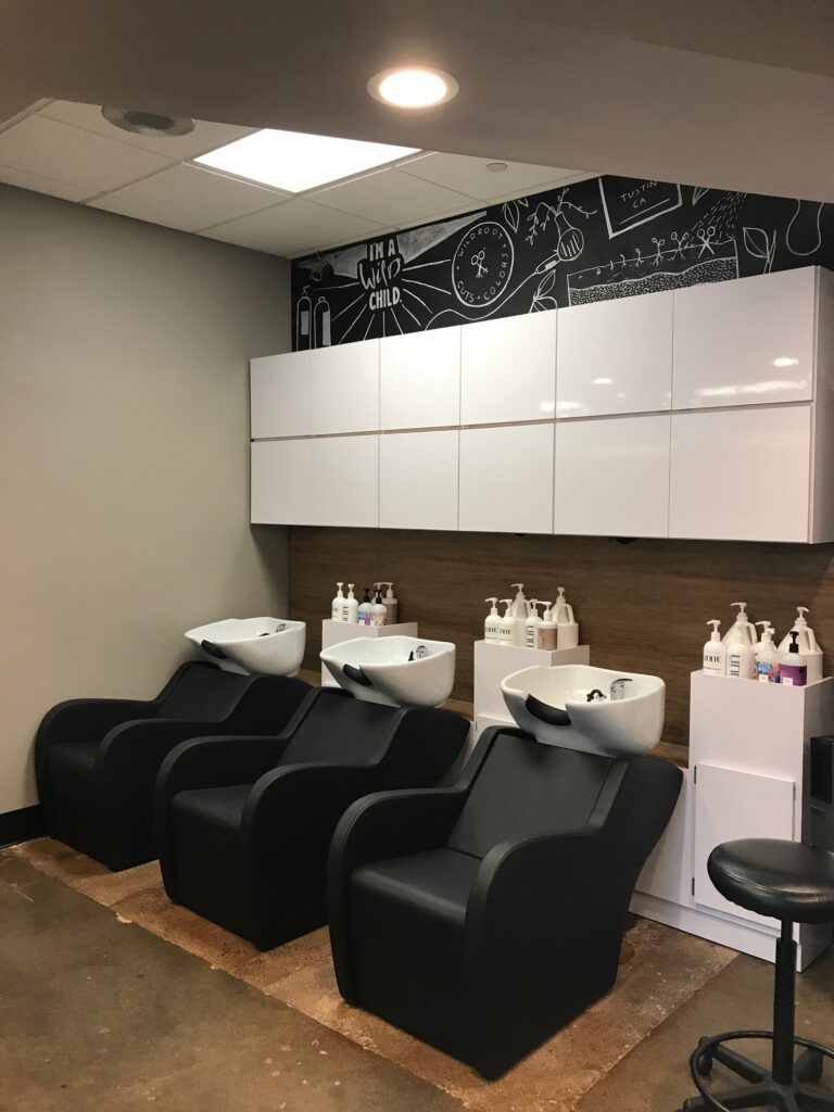 Three black salon chairs with white washbasins, white cabinets, and wall art.