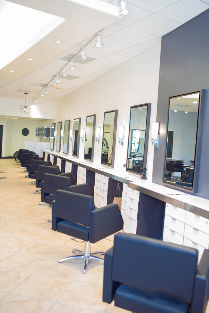 Salon with row of black styling chairs, mirrors, and tiled floor.