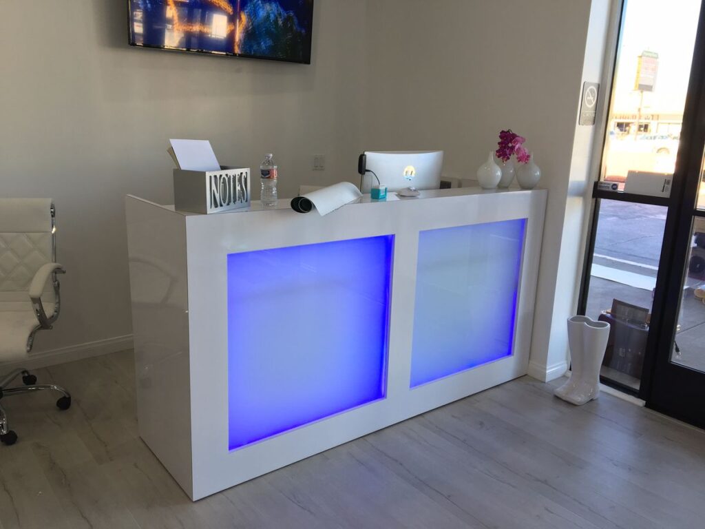 Reception desk with blue-lit panels, white chair, and decorative vases near window.