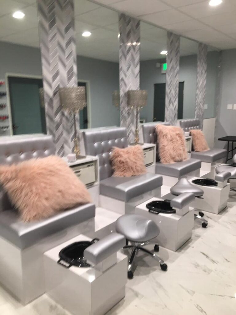 Salon pedicure stations with silver seats, pink pillows, and foot baths on tiled floor.